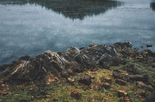 A vertical shot of rocks near the water refecting the mountain in the background
